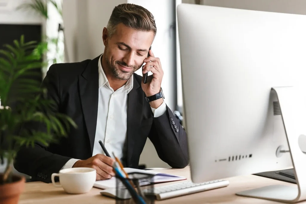 businessman talking on cell phone while working on computer in office
